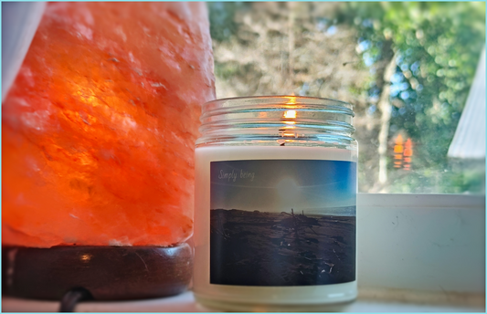 good smelling scented candle made of natural hand poured wax in glass reusable jar. beach sunset driftwood and sunbeams design. consciousness message reads 'simply being'