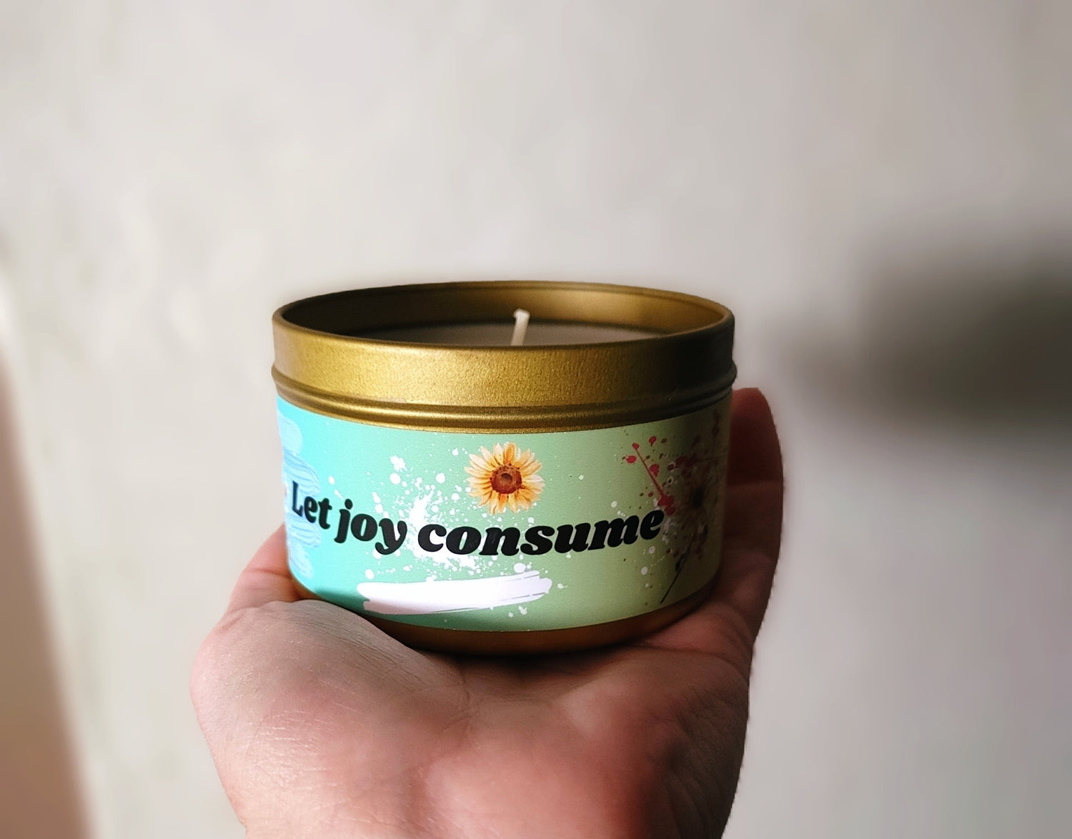 gold candle in steel tin with 5 good smelling scent options and two size choices. This natural candle has original vibrant floral and paint splattered design and motivational quote, let joy consume