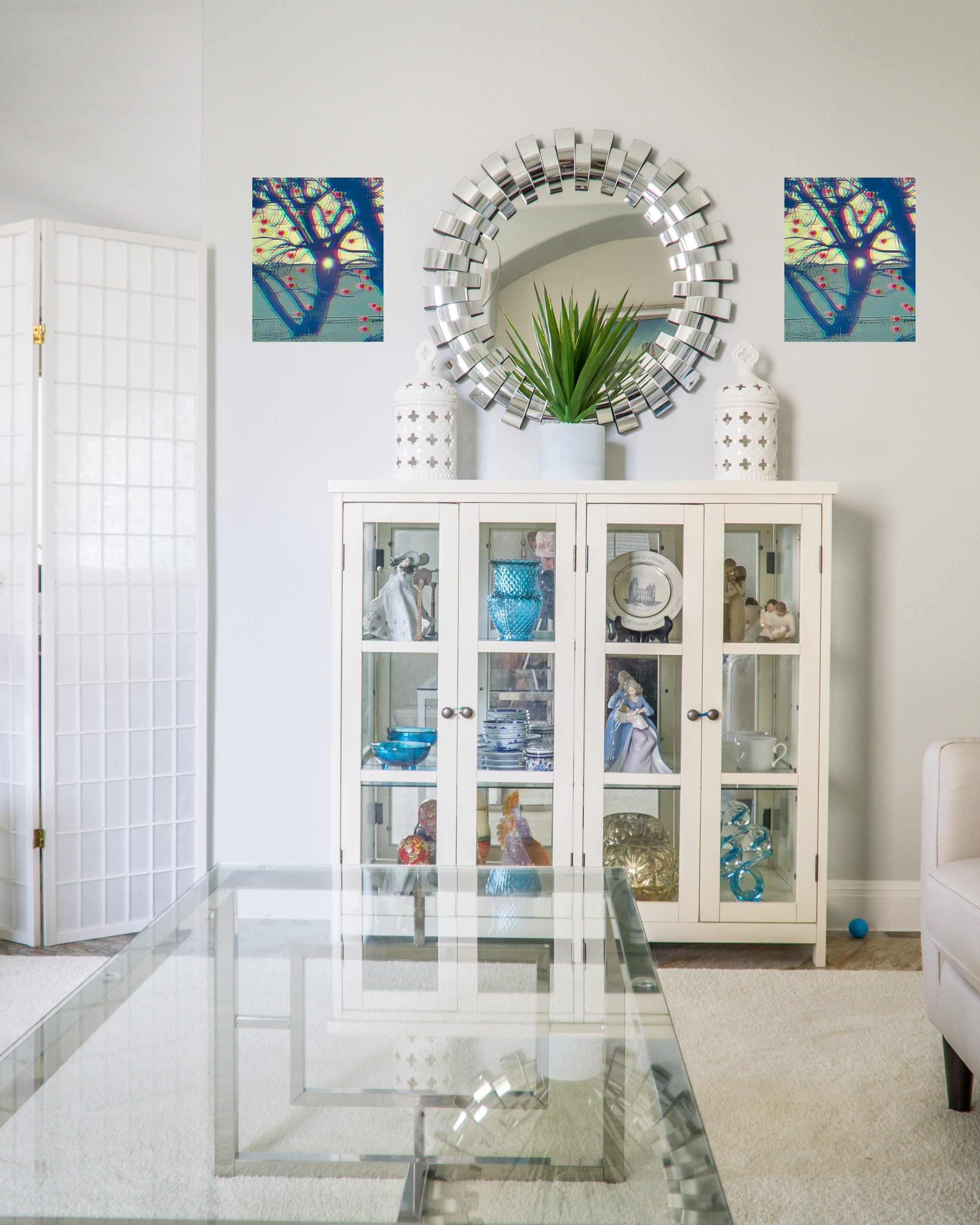 Trendy living room with a glass display cabinet, lux mirror and coffee table, and original wall art design with blue hue and sun peeking through a tree growing hearts